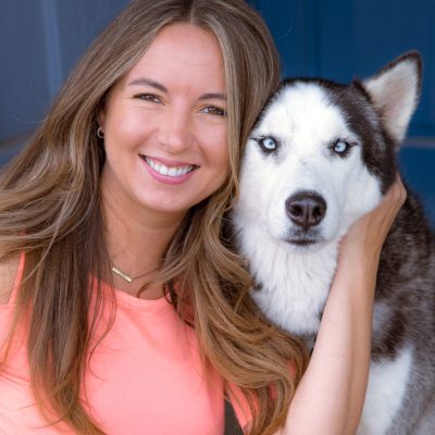 A woman smiling while posing with a Siberian Husky dog with blue eyes.
